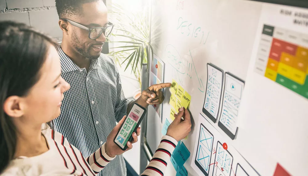 Hombre y Mujer ubicando notas adhesivas en un tablero que ilustra un proyecto