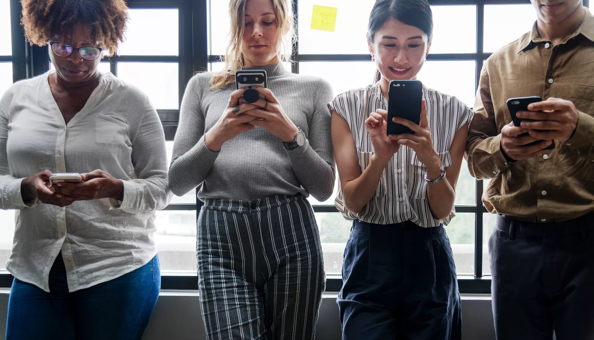 cuatro personas en de pie mirando cada uno su teléfono móvil