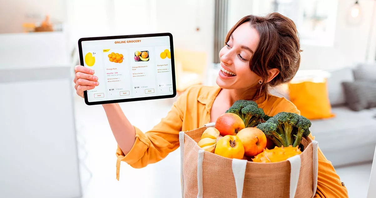 Mujer con un paquete de frutas adquirido a traves de una tablet, representa el mobile commerce como tendencia en crecimiento citado en este artículo de webkreativo