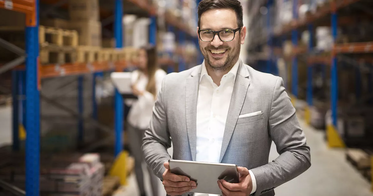 Imagen de Empresario sonriendo en una bodega con una Tablet en las manos, para ilustrar la facilidad de manejar una empresa en la red a través del ecommerce